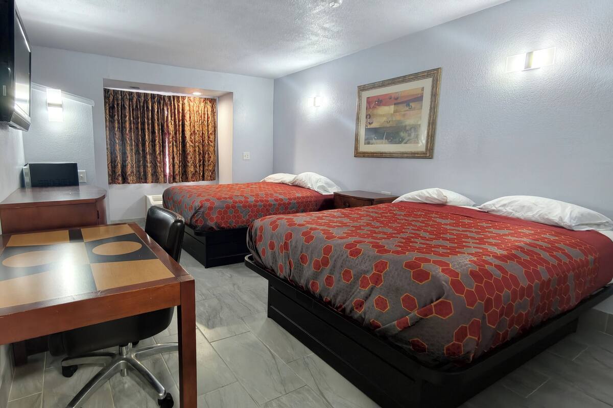 Ein Hotelzimmer mit zwei Betten, einem Schreibtisch, einem Sessel, einem Fernseher und einem Bild an der Wand.
