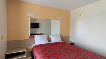 A hotel room with a bed, a TV, a mirror, and a small shelf.