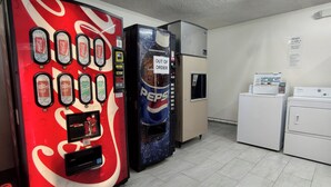 Máquinas expendedoras de Coca-Cola y Pepsi, un refrigerador y un electrodoméstico blanco pequeño en una habitación con suelo de baldosas.