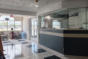 A reception area with a check-in counter, chairs, a small table, and a window with a view. - Classic Inn San Marcos, TX (San Marcos)