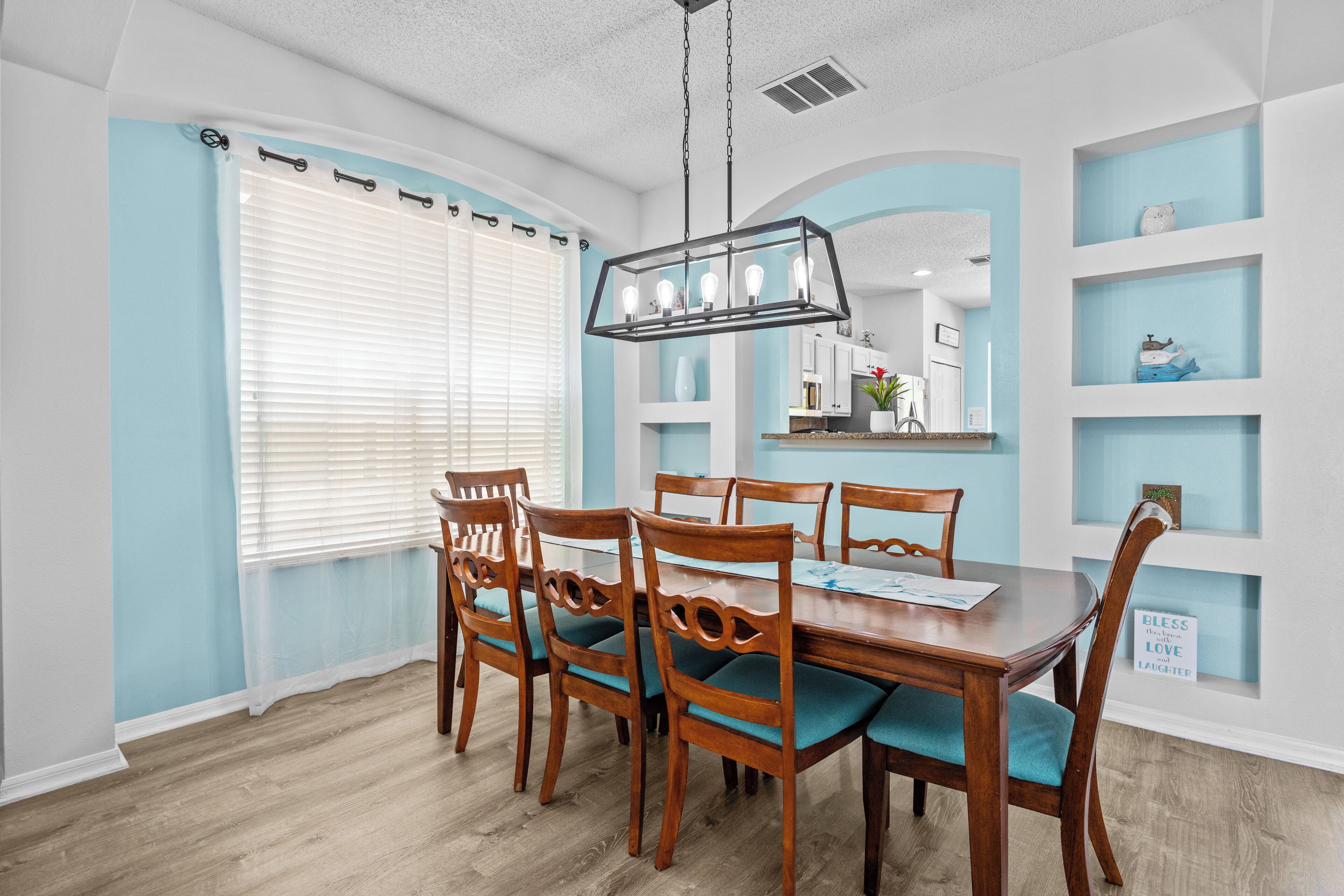 A dining area with a wooden table and chairs, a chandelier, and light blue walls.