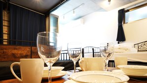 A dining table set with white plates, bowls, and wine glasses, with a bed and window in the background. - Laffitte Hirai Condominium Hotel (Tokyo)