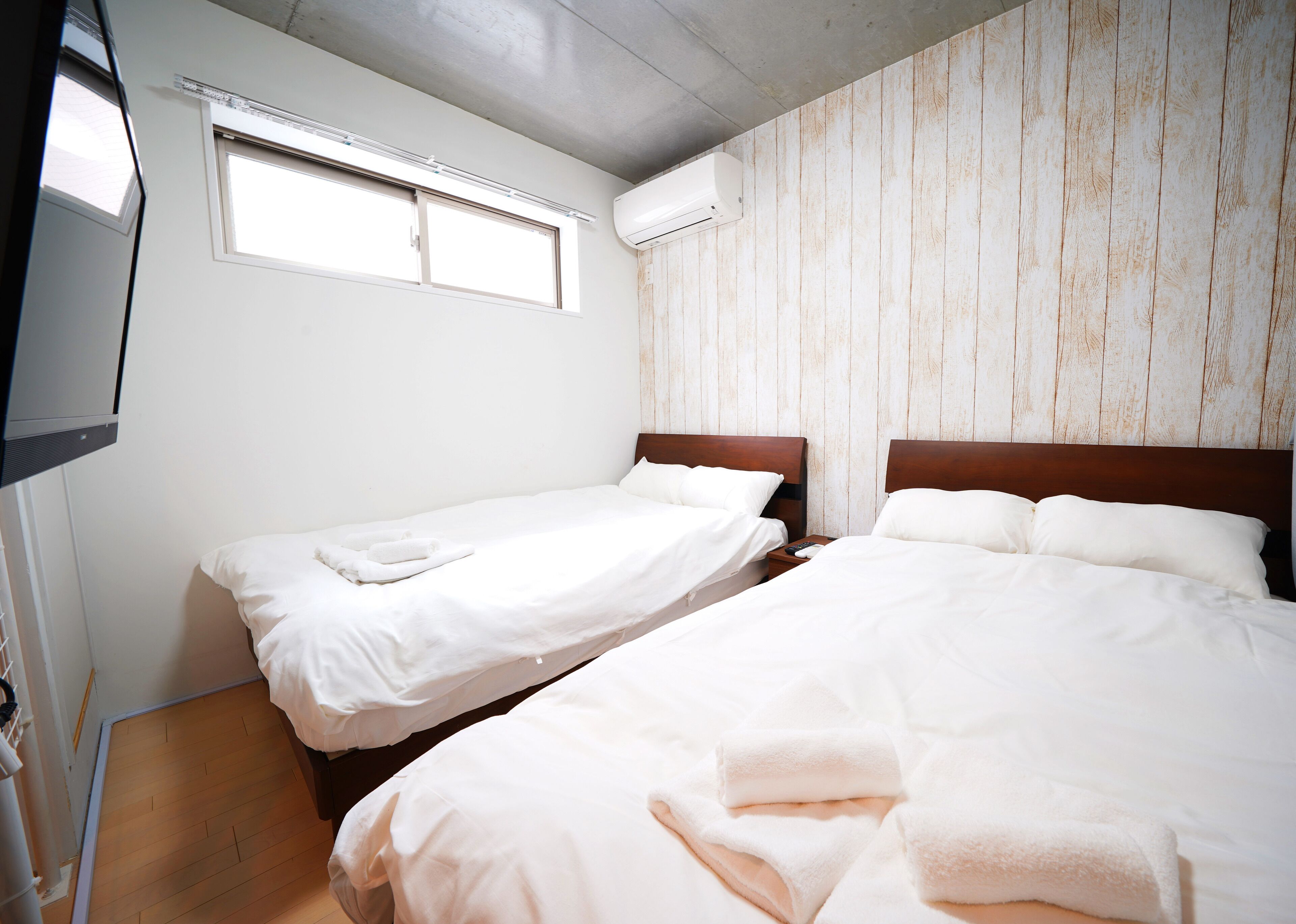 A hotel room with two single beds, a television, and an air conditioning unit.