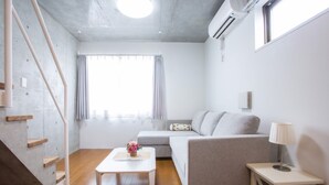 A modern living room with a sofa, a coffee table, a lamp, and a staircase. - Laffitte Hirai Condominium Hotel (Tokyo)