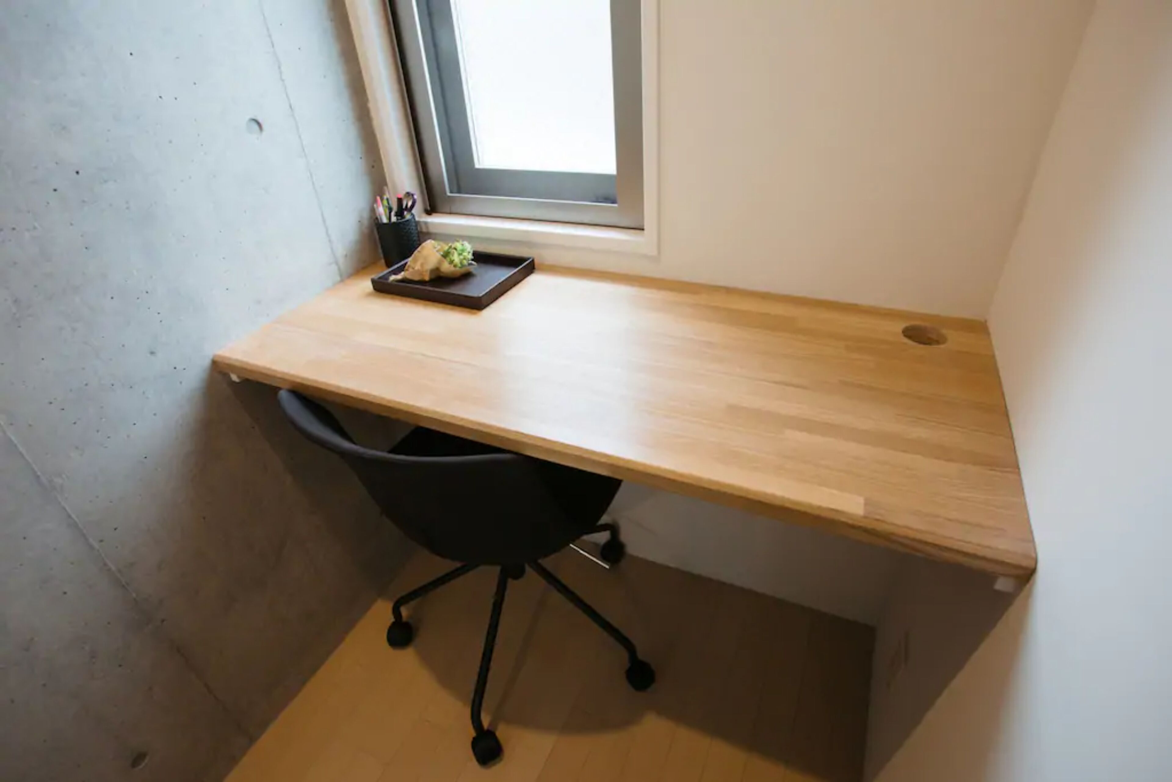 A small office space with a wooden desk, a black office chair, and a window with blinds.