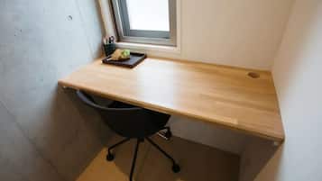 A small office space with a wooden desk, a black office chair, and a window with blinds.