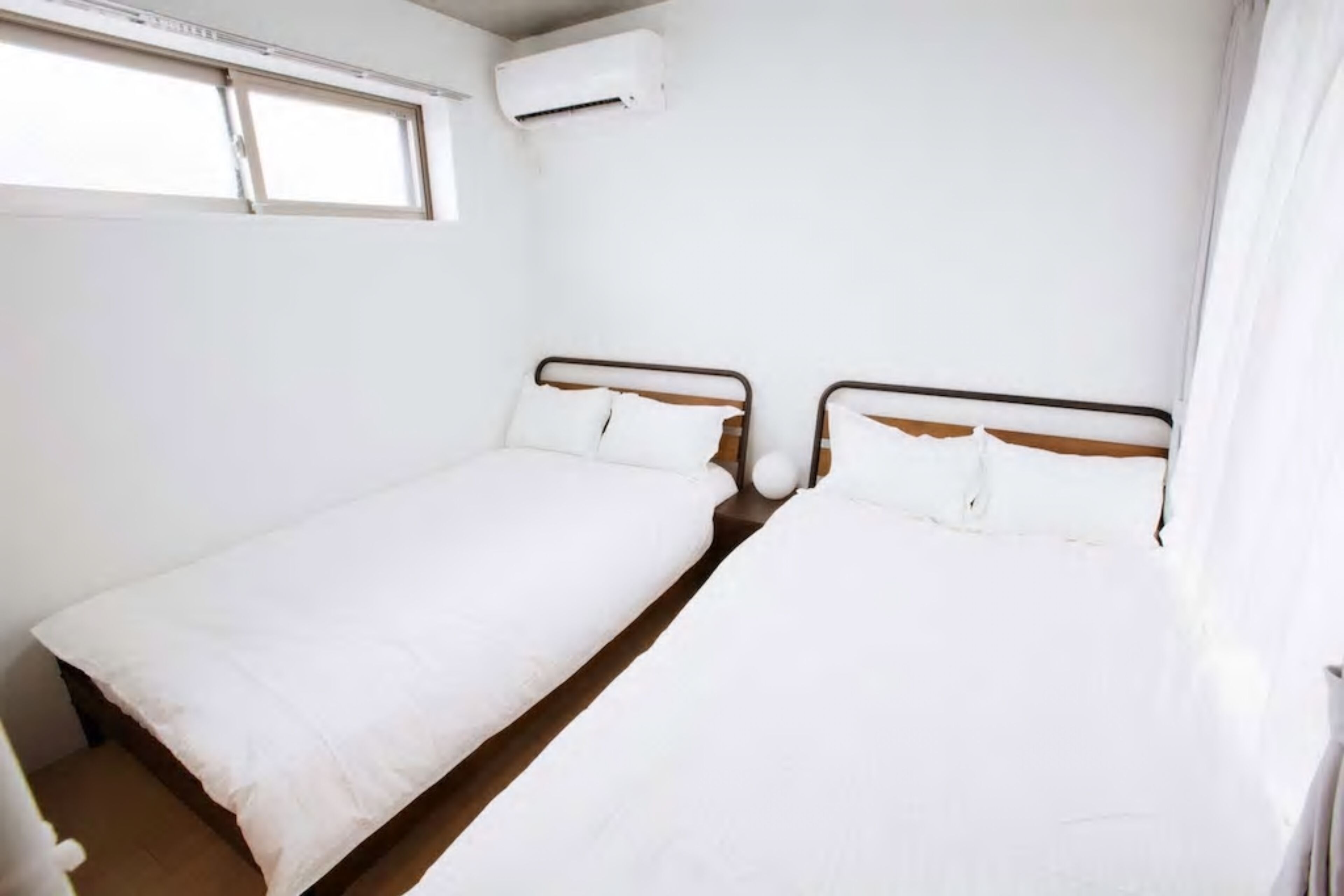 Een kleine, schone kamer met twee eenpersoonsbedden, een raam en een airconditioning.
