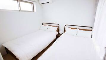 Een kleine, schone kamer met twee eenpersoonsbedden, een raam en een airconditioning.