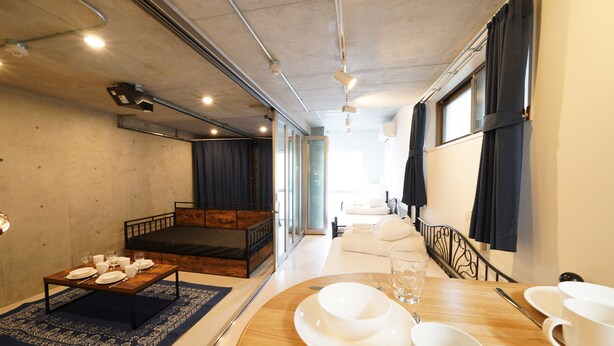 A modern room with a wooden bed, a dining table set for two, and a view of a balcony. - Laffitte Hirai Condominium Hotel (Tokyo)