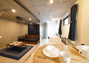 A modern room with a wooden bed, a dining table set for two, and a view of a balcony. - Laffitte Hirai Condominium Hotel (Tokyo)
