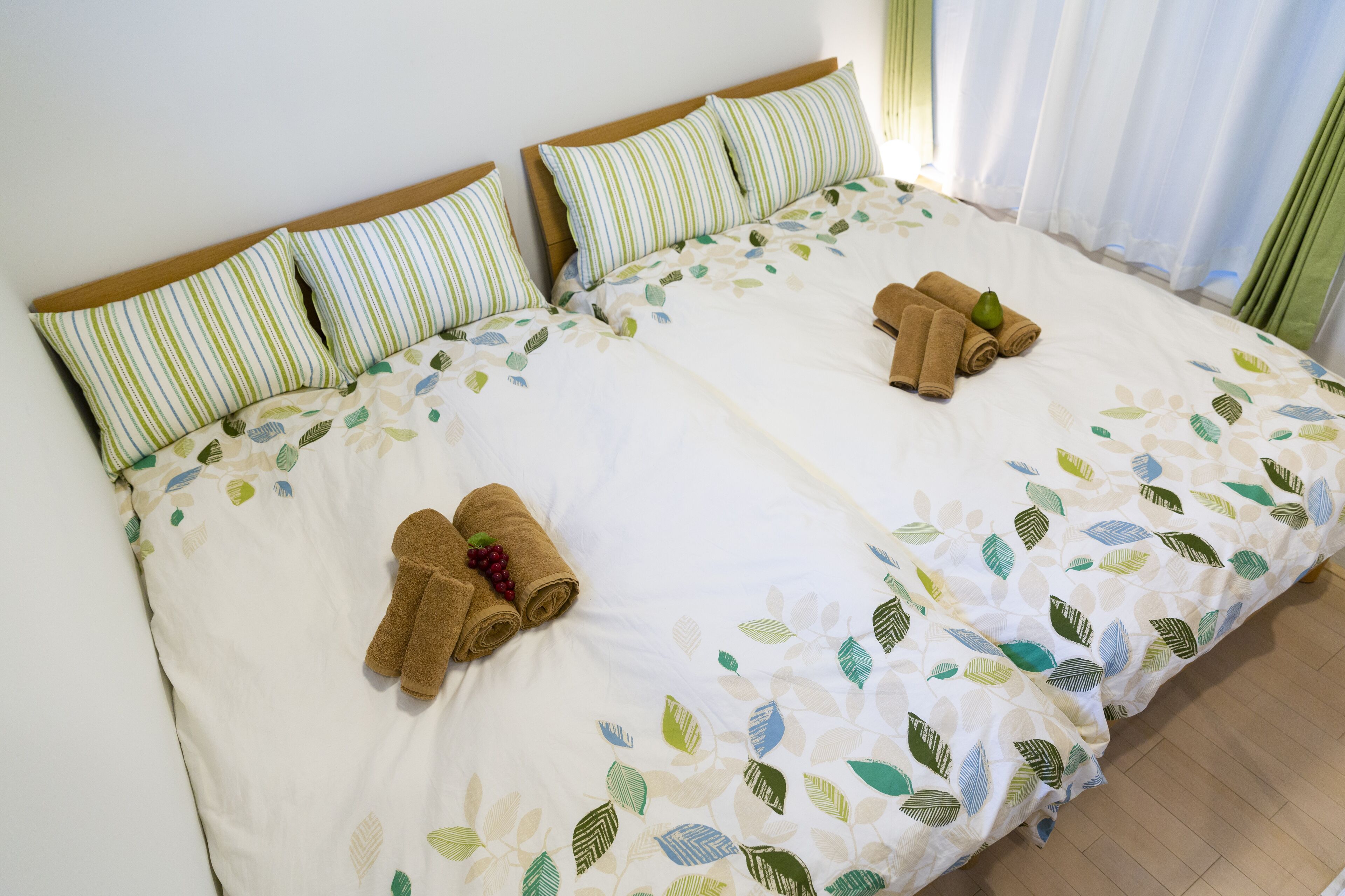 Una cama doble con almohadas a rayas, una colcha estampada con motivos de hojas y toallas enrolladas sobre la cama.