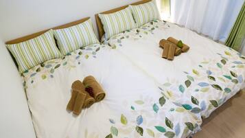 Una cama doble con almohadas a rayas, una colcha estampada con motivos de hojas y toallas enrolladas sobre la cama.