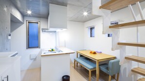 A modern kitchen with a built-in island, a dining area with a wooden table and blue chairs, and a small window. - Laffitte Hirai Condominium Hotel (Tokyo)