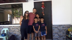A family of five standing in front of a house with a brick wall and a large window. - Bohol Sweet Home B&B (Guindulman)