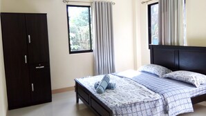 A bedroom with a bed, a wardrobe, and two windows with curtains. - Bohol Sweet Home B&B (Guindulman)