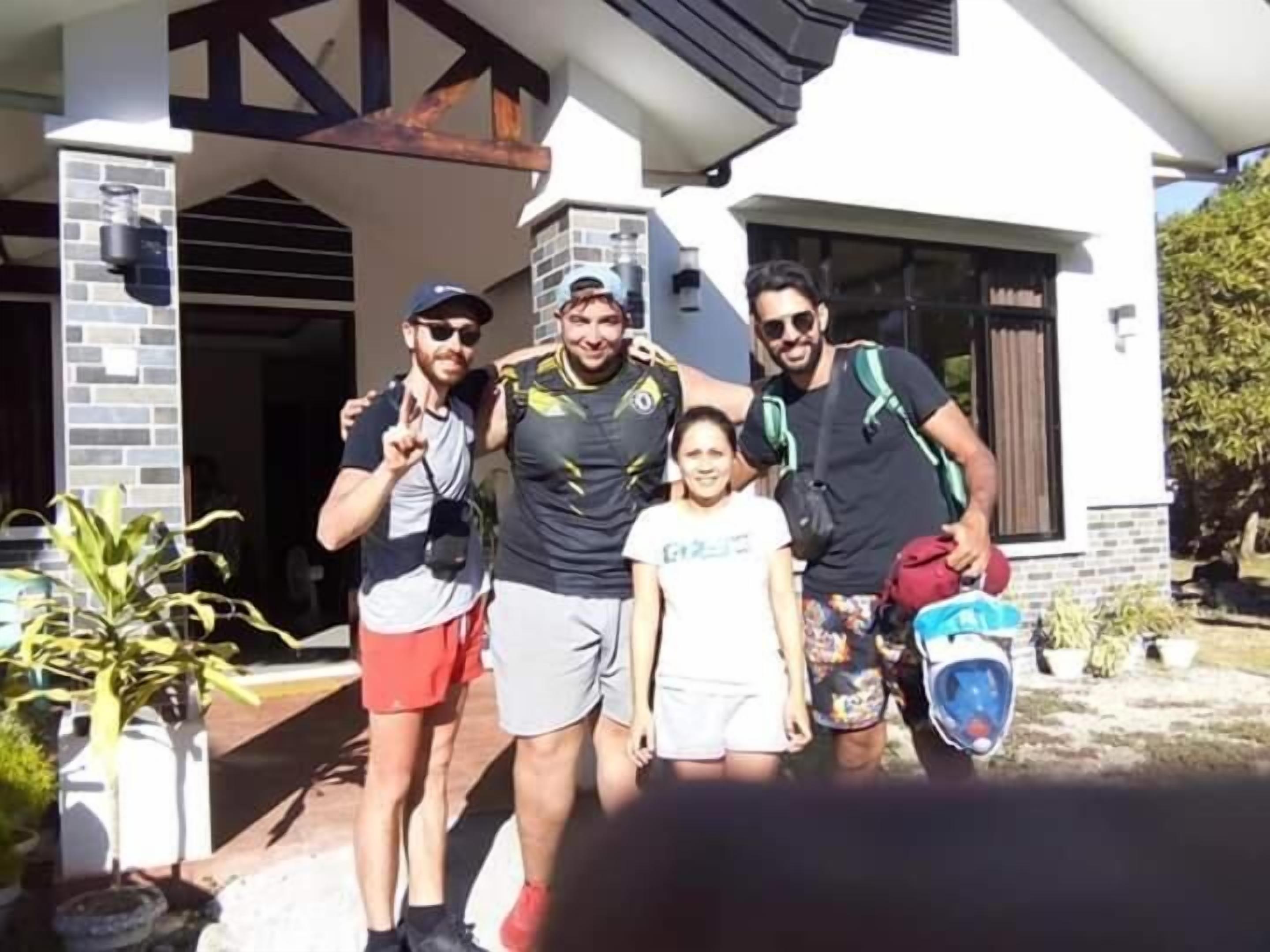 Un grupo de personas de pie frente a una casa con fachada de ladrillo y porche cubierto.