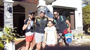 Un grupo de personas de pie frente a una casa con fachada de ladrillo y porche cubierto.