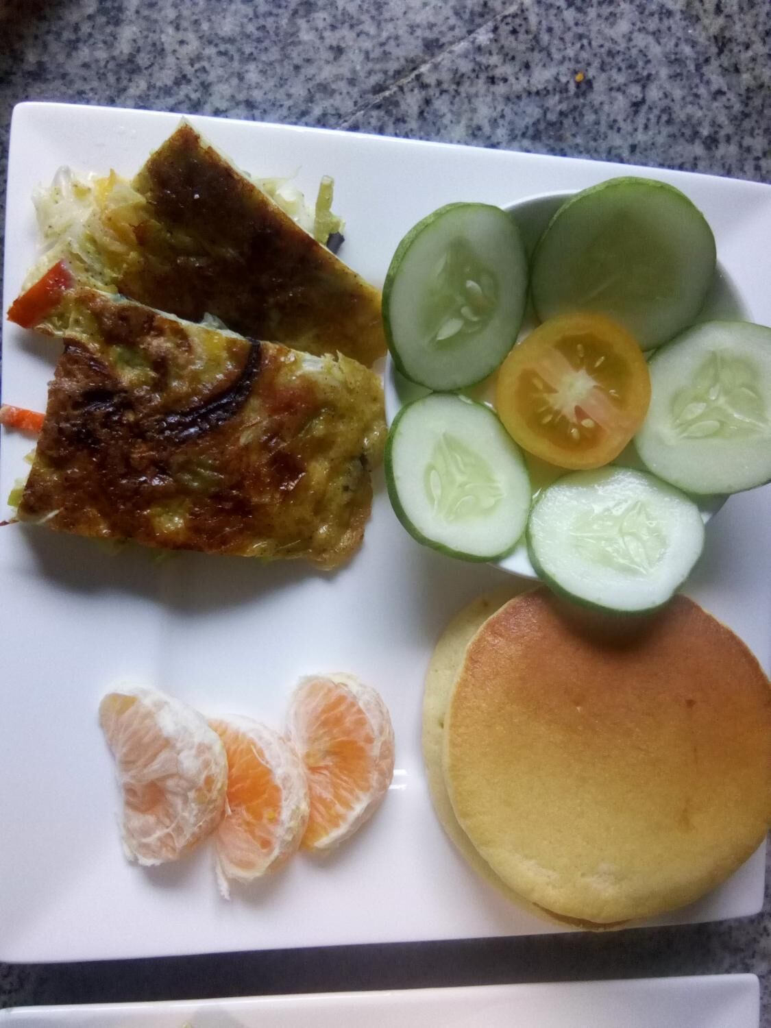 A plate with a grilled dish, sliced cucumbers, tomatoes, and a pancake.