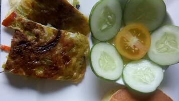 A plate with a grilled dish, sliced cucumbers, tomatoes, and a pancake.