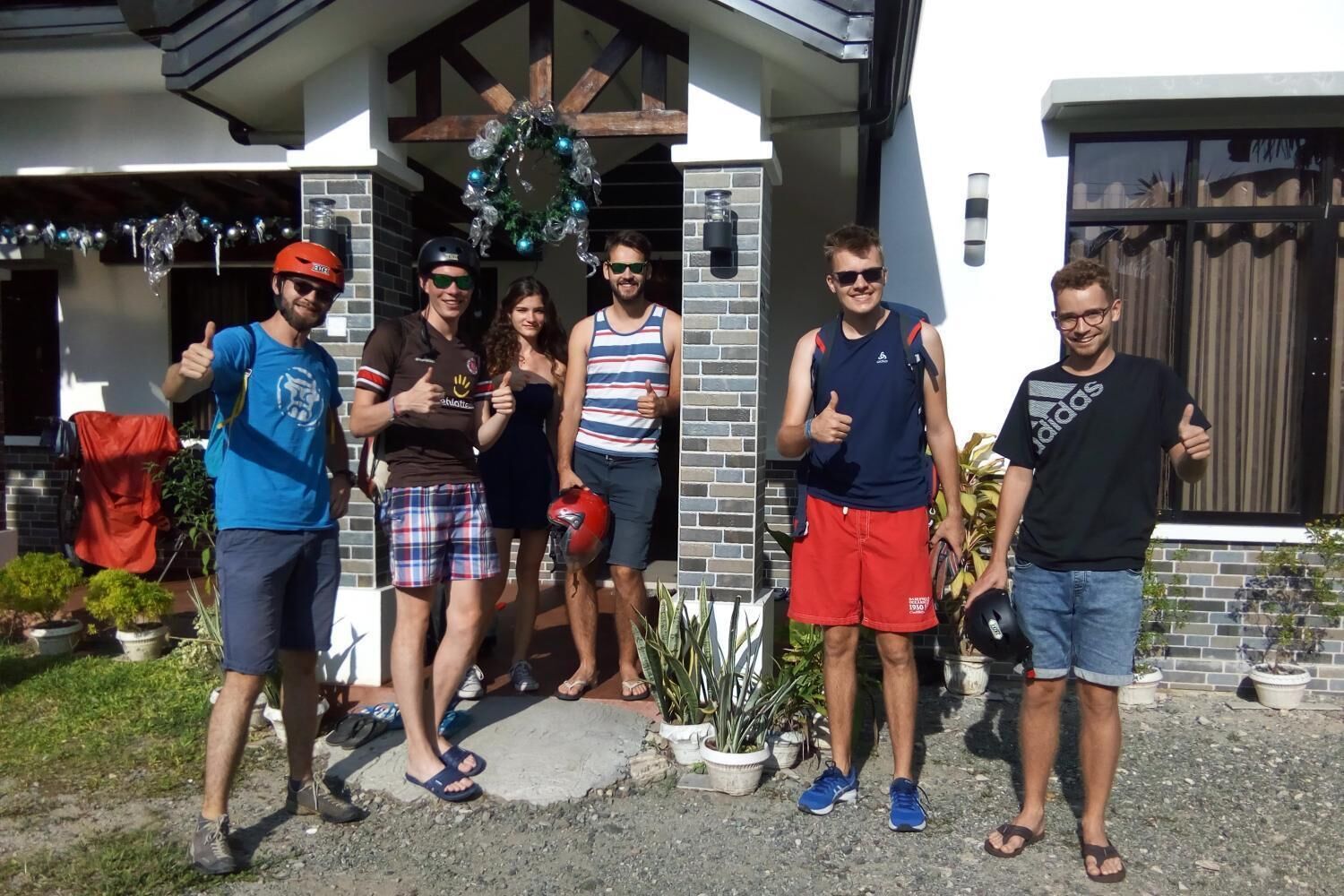 Un gruppo di persone in piedi di fronte a una casa con facciata in mattoni e portico in legno.