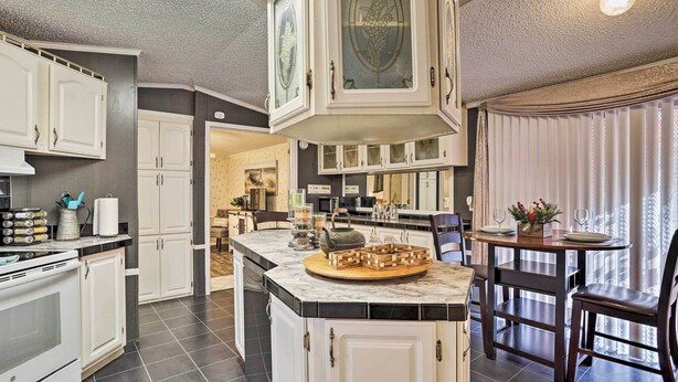 Una cocina con armarios blancos, encimera de mármol y comedor con mesa y sillas.