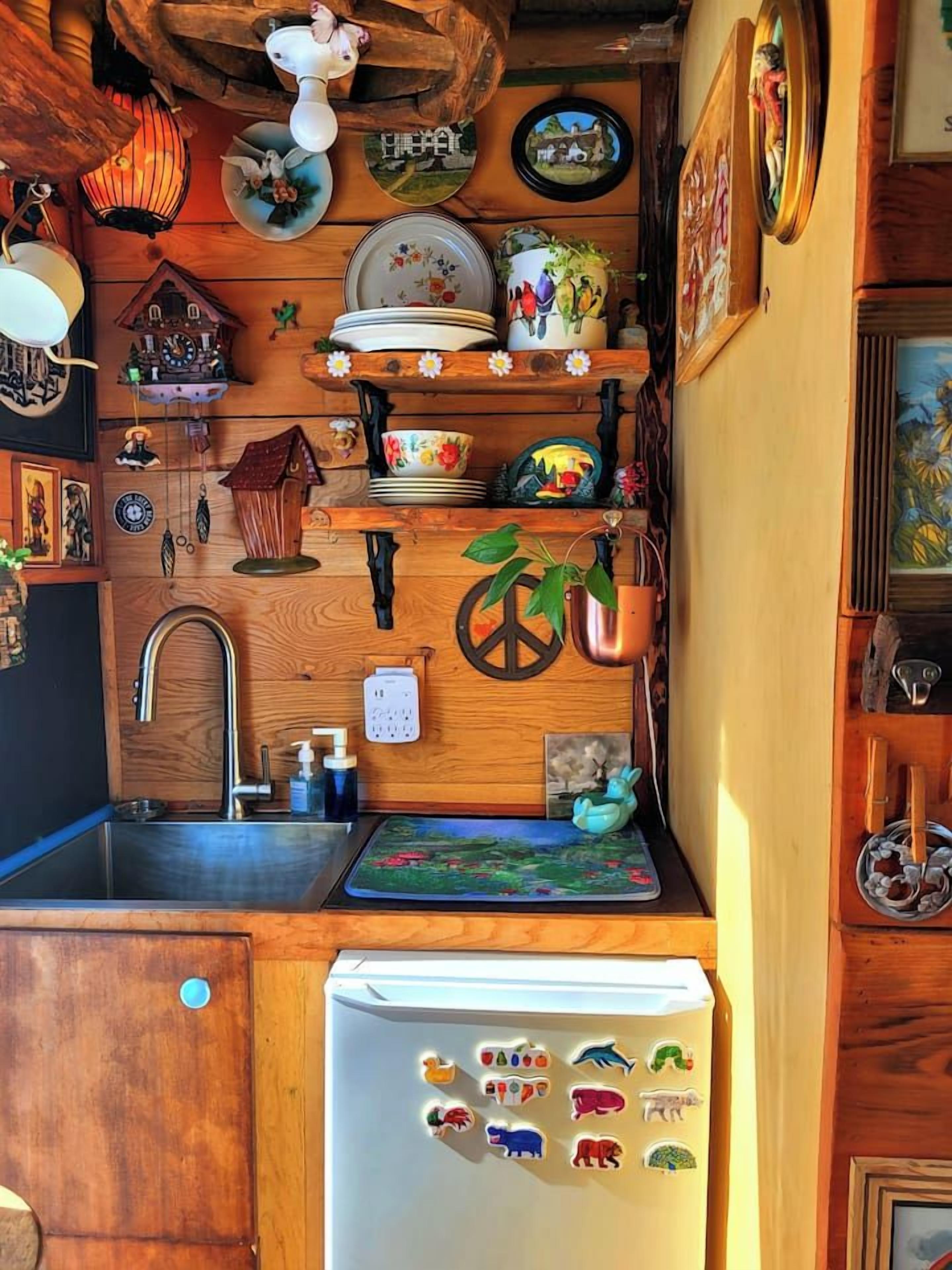 A kitchen with wooden cabinets, a sink, a refrigerator with magnets, and various decorative items on the walls.