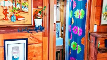 A wooden interior with a door leading to a bathroom, a framed picture of a landscape, and a shower curtain with a floral pattern.
