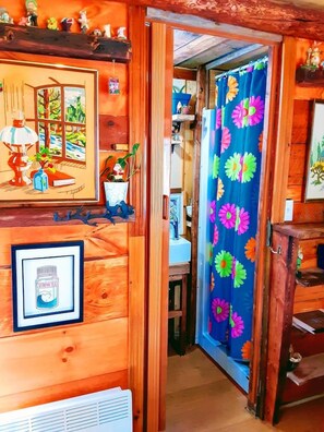 Un intérieur en bois avec une porte donnant accès à une salle de bain, un tableau encadré représentant un paysage et un rideau de douche orné d’un motif floral.