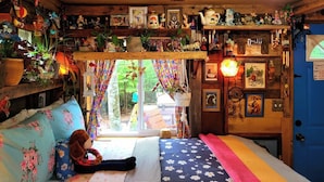 Een gezellige kamer met een bed, een raam met gordijnen en diverse decoraties aan de wanden.