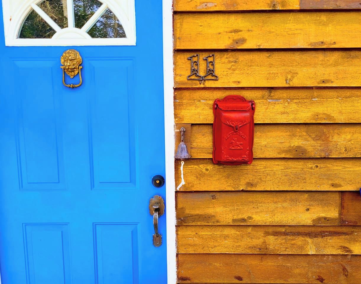 A blue door with a brass knocker and a red mailbox on a wooden wall.