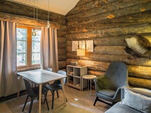 A log cabin interior with a dining table, chairs, a sofa, a lamp, and a radio on a shelf.