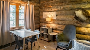 Een knus blokhutinterieur met een eettafel, stoelen, een bank en een lamp.