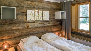 Een knus houten blokhutkamer met een bed, een bedlamp en een raam met uitzicht op bomen.