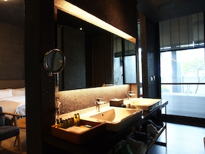 Habitación de hotel con un espejo grande, dos lavamanos, una silla y una cama.