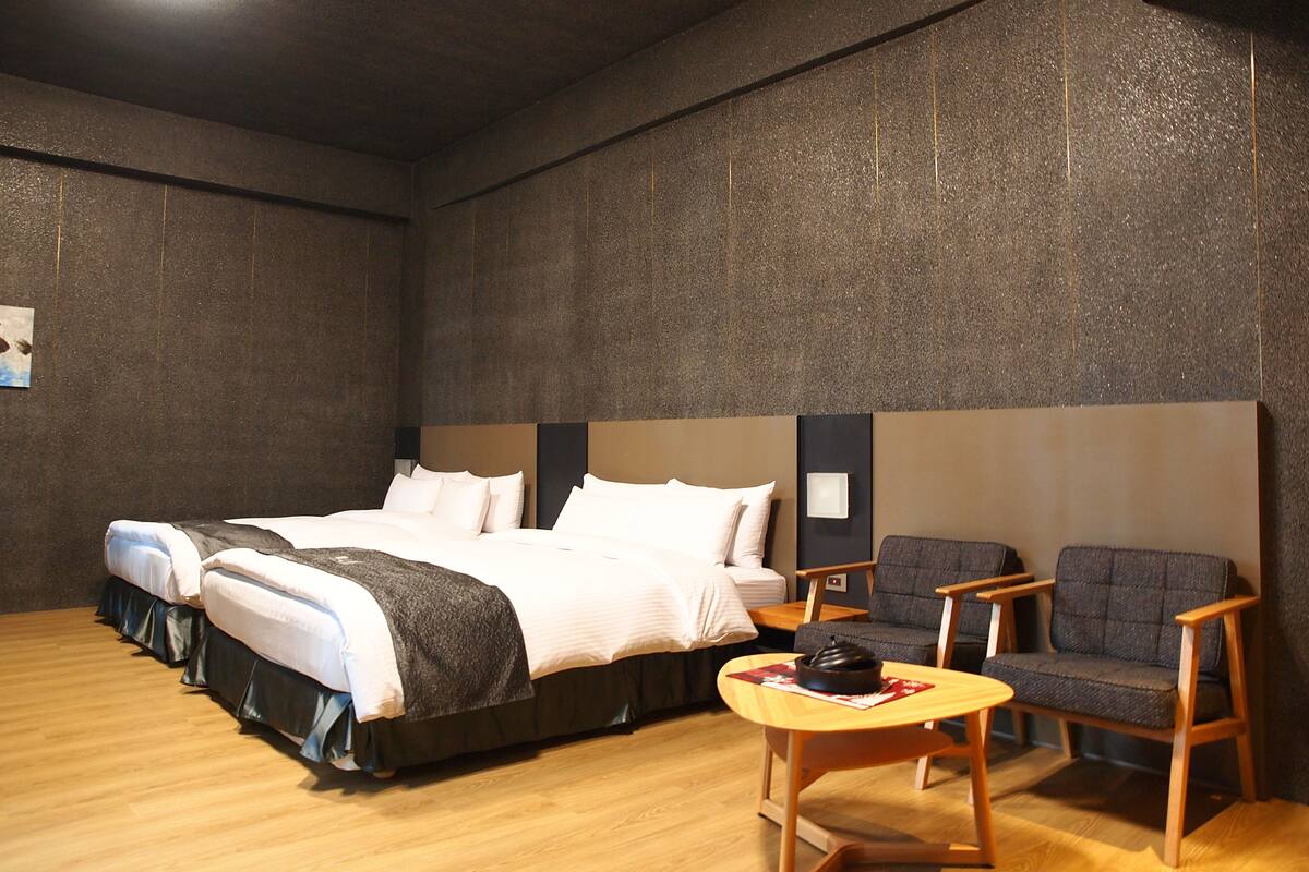 Une chambre d’hôtel avec un grand lit, deux chaises, une petite table et un mur à texture.