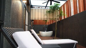 Un área de descanso al aire libre moderna con una bañera grande, sillones de relax y una estructura de pérgola.