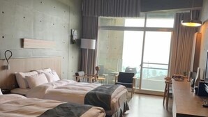 Habitación de hotel con dos camas, un escritorio y un ventanal grande.