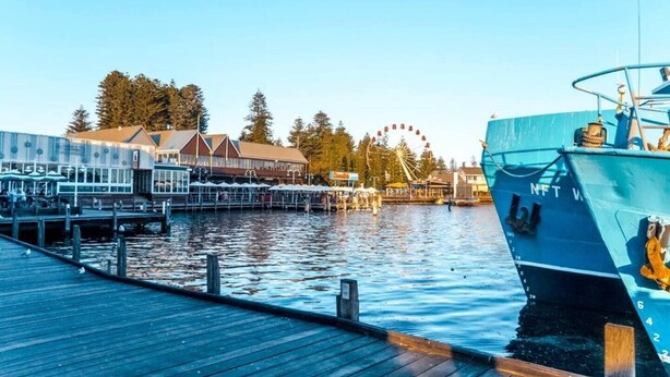 A waterfront dock with a large blue boat, a pier with a building, and a Ferris wheel in the background. - Wake up to sweeping harbour views in this modern, split-level apartment located between Fishing Boat Harbour and Challenger Harbour. Whether you're a couple, a family, or here on business, this peaceful retreat offers the best of coastal charm and ci (Fremantle)