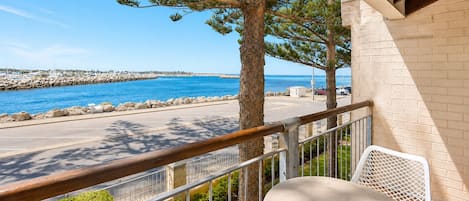 A balcony with a view of the sea, a chair, and a table.