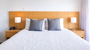 A hotel room with a large bed, two bedside lamps, a nightstand with a radio, and a wooden headboard. - Wake up to sweeping harbour views in this modern, split-level apartment located between Fishing Boat Harbour and Challenger Harbour. Whether you're a couple, a family, or here on business, this peaceful retreat offers the best of coastal charm and ci (Fremantle)