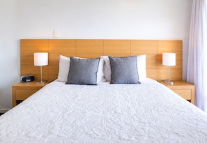 A hotel room with a large bed, two bedside lamps, a nightstand with a radio, and a wooden headboard. - Wake up to sweeping harbour views in this modern, split-level apartment located between Fishing Boat Harbour and Challenger Harbour. Whether you're a couple, a family, or here on business, this peaceful retreat offers the best of coastal charm and ci (Fremantle)
