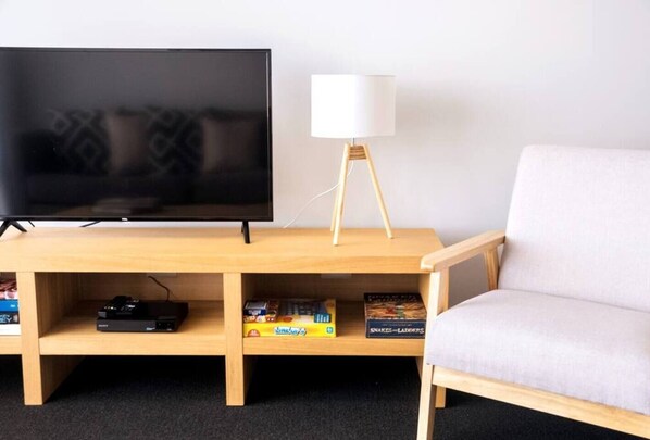 A modern living room with a flat-screen TV on a wooden stand, a white floor lamp, and a gaming console. - Wake up to sweeping harbour views in this modern, split-level apartment located between Fishing Boat Harbour and Challenger Harbour. Whether you're a couple, a family, or here on business, this peaceful retreat offers the best of coastal charm and ci (Fremantle)