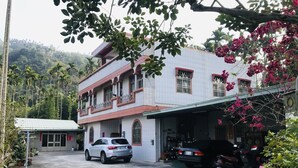 A two-story building with a garage, surrounded by greenery and parked vehicles. - Hua Yi Homestay (Gukeng)