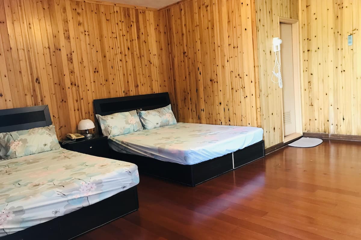 A room with two beds, wooden walls, and a wooden floor.