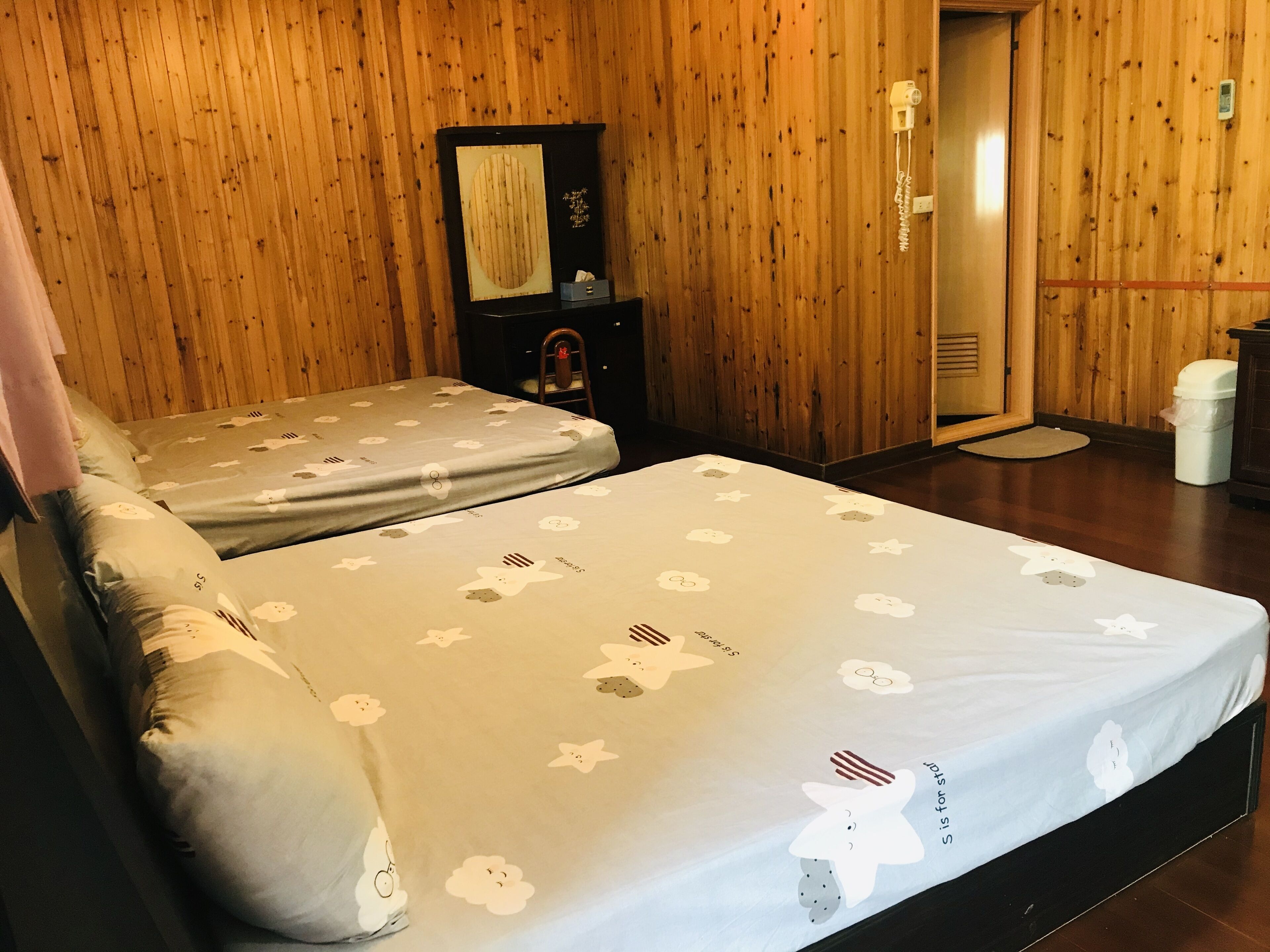 Een kamer met twee bedden, houten wanden, een klein kastje en een telefoon.
