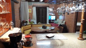 Ein gemütliches Wohnzimmer mit einer Couch, einem Couchtisch und einem Fernseher. Auf dem Tisch liegen verschiedene Gegenstände, darunter ein Einmachglas und ein Buch.