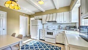 A kitchen with white cabinets, a refrigerator, stove, and a microwave. There is a blue patterned rug on the floor. - Oceanside Beach House in Pvt Beach Community! (Mantoloking)
