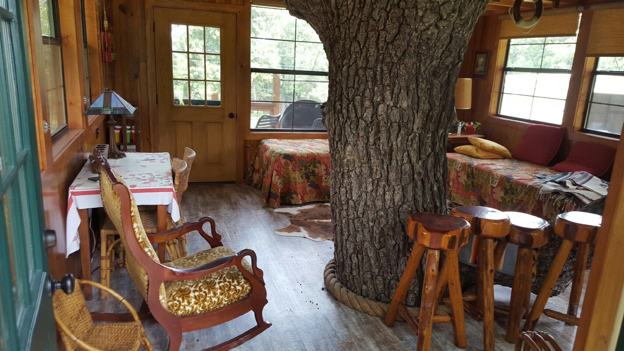 Interior rústico de una cabaña con comedor, un gran tronco de árbol y una cama acogedora con una manta colorida.