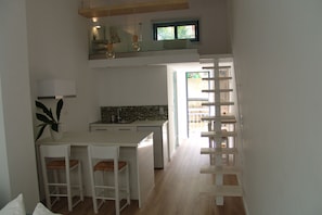 A modern kitchen with a central island, bar stools, and a wooden staircase leading to a balcony.