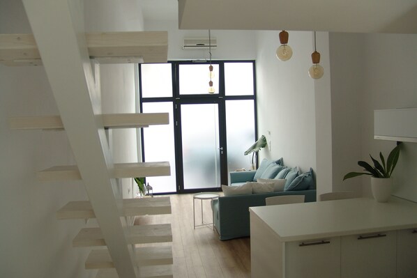 A modern living room with a staircase, a sofa, and a dining area.